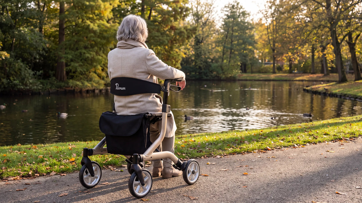 Parvum SuperLight in champagne by a pond in the park; a woman with gray hair sits on the rollator, her back against the backrest.