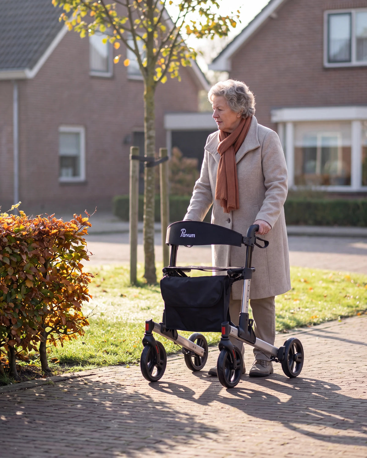 Parvum Riva in gray on the sidewalk along a beech hedge; a woman in a wool coat stops for a moment.